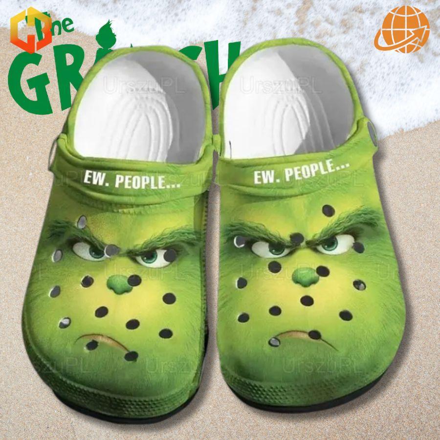 Ew People Grinch Crocs Shoes with detailed Grinch face and "EW. PEOPLE..." strap, displayed on a snowy beach with "The GRINCH" text visible.