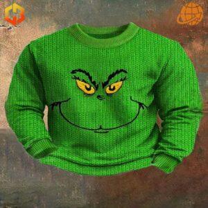 Bright green knit Grinch Face Christmas Sweater with yellow eyes and sly smile design on rustic background.