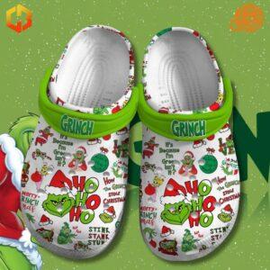 Close-up of Grinch Crocs featuring festive designs, "HO HO HO" text, and green straps on a snowy green backdrop.