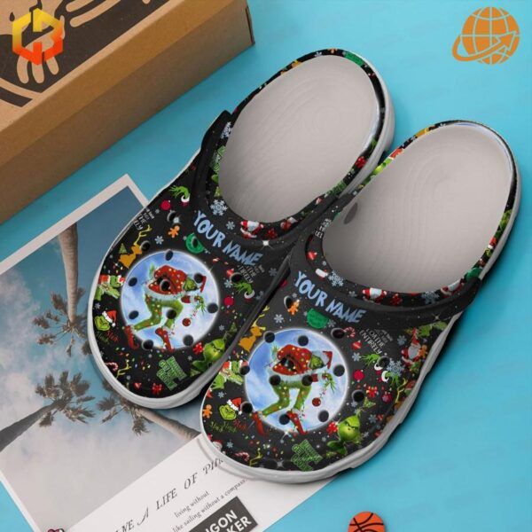 Top view of Grinch-themed Crocs clogs with box and decorative items on blue background.