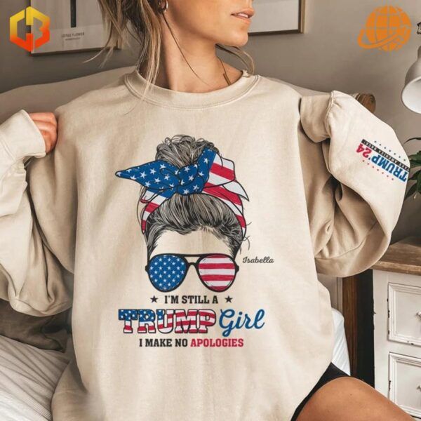 A beige sweatshirt with a patriotic design featuring a woman’s silhouette wearing sunglasses and a headband with an American flag pattern, paired with the bold text, 'I’m Still A Trump Girl, I Make No Apologies,' and 'Trump '24' on the sleeve.