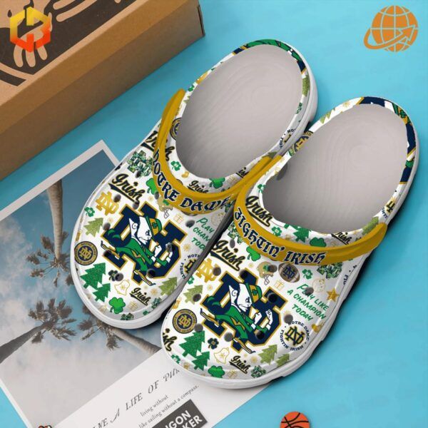 Notre Dame Fighting Irish Crocs Shoes with a vibrant design, displayed on a blue background next to a box and a postcard.