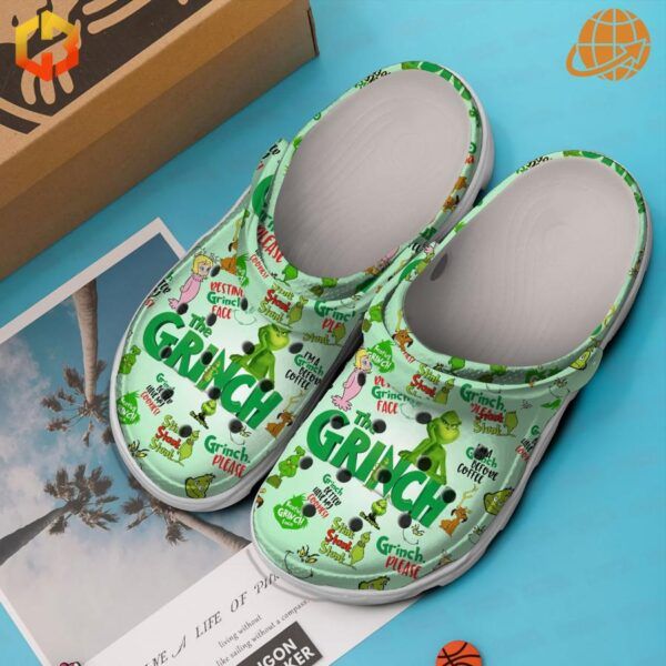 Green The Grinch Clogs with Grinch-themed graphics, placed beside a photo of palm trees on a blue surface.