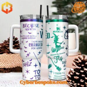 The image showcases two white Stanley tumblers with handles, each featuring unique designs inspired by the Broadway musical 