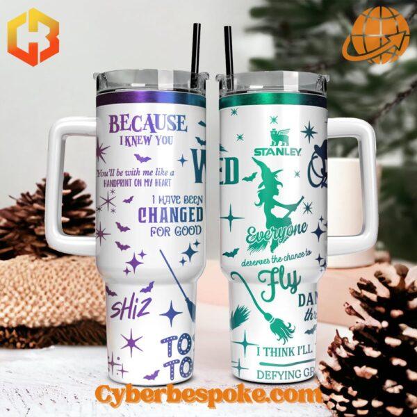 The image showcases two white Stanley tumblers with handles, each featuring unique designs inspired by the Broadway musical "Wicked."